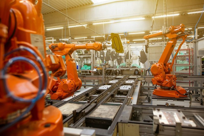 Orange industrial robot arms working in a fenced robot cell beside conveyor tracks